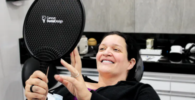 woman patient seeing her smile in a mirror after a complete smile makeover at cancun dental design