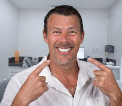 A smiling caucasian man pointing to his perfect smile, showcasing successful full-arch dental implant restoration