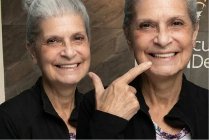 Happy female patient pointing to her full-arch dental restoration, showcasing the aesthetic results of All-on-X dental implants in a professional clinic setting.