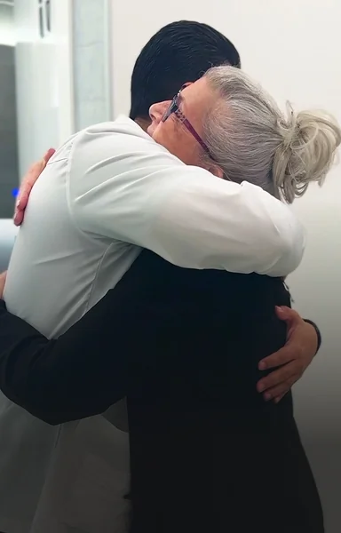 Happy senior female patient warmly hugging her dentist inside the clinic.