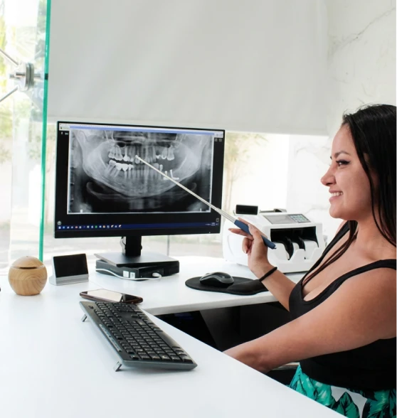 Female dental specialist pointing at a panoramic digital 3D CBCT scan of a patient's teeth on a computer monitor during an implant evaluation.